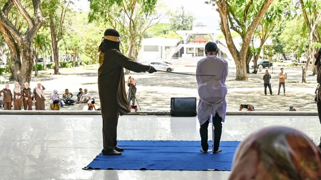 Two gay men grimace in pain as they are brutally whipped in public